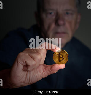 Senior uomo esaminando un bitcoin per la lunghezza del braccio Foto Stock