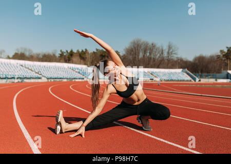 Una bella ragazza di sport in abbigliamento sportivo nero sta facendo un warm-up prima di praticare sport presso lo stadio. Il concetto di uno stile di vita sano. Foto Stock