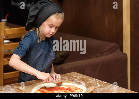 Bambina cuocere in uniforme si prepara la pizza in cucina. Foto Stock