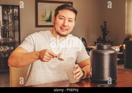 Uomo di andare a versare una porzione della proteina di siero di latte presso la coppa di miscelazione. Post Allenamento proteine. Foto Stock