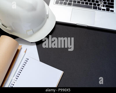 Piatto bianco laici hard casco di sicurezza con laptop, notebook, carta e matita per lavoratore di ingegneria su sfondo nero in vista superiore con lo spazio. Foto Stock