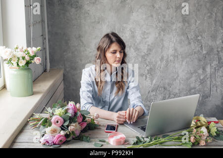Il concetto di ordine di prelievo e consegna. tavolo di lavoro in negozio di fiori. Ragazza assistant o il proprietario in floral design studio, rendendo le decorazioni e le modalità. Foto Stock