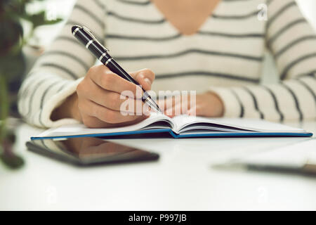 Azienda giovane donna seduta a tavola e la scrittura nel notebook. Sul tavolo è lo smartphone e tablet. Lavoro freelancer, scrivere nuove idee Foto Stock