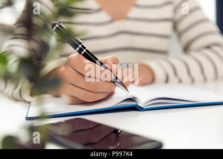 Azienda giovane donna seduta a tavola e la scrittura nel notebook. Sul tavolo è lo smartphone e tablet. Lavoro freelancer, scrivere nuove idee Foto Stock