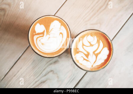 Due bicchieri di cappuccino con latte art su un tavolo di legno. Close up, vista dall'alto. Foto Stock