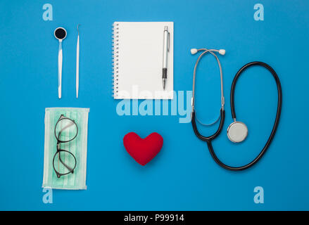 Table top visualizza immagine aerea di accessori del settore sanitario e medico di fondo concetto.cuore rosso & stetoscopio con oggetti essenziali su carta blu.Flat l Foto Stock