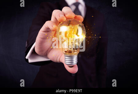 Un elegante lavoratore di ufficio tenendo un giallo luce scintillante la lampadina in mano mentre si lavora nella parte anteriore di sfondo blu scuro concetto. Foto Stock