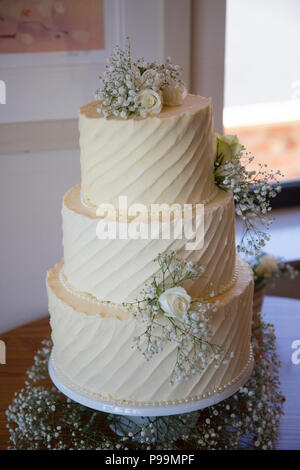 Tre livelli di torta nuziale coperta in glassa di crema di burro e fiori reale Foto Stock