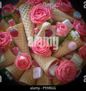 Bouquet composto da fiori di rosa rose, waffle coni, dolciumi e marshmallows su sfondo scuro Foto Stock