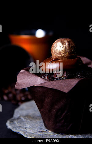 Muffin al cioccolato e rabboccato con superficie liscia di glassa di cioccolato e oro artigianale di pasticceria e presentati su un Cornish ardesia Foto Stock