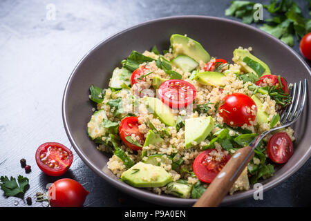 Cibo vegan. La quinoa con insalata di spinaci, avocado e pomodori in pietra scura tabella. Close up. Foto Stock