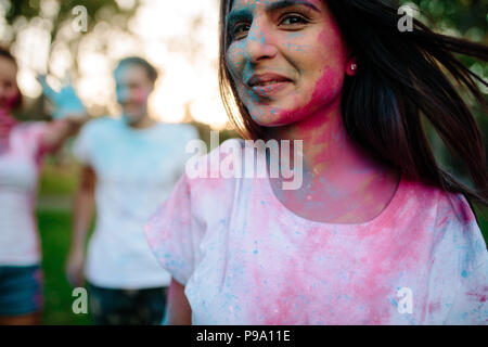 Giovane donna faccia cosparsa di colori. Ragazza che gioca con gli amici alla schiena durante il festival dei colori. Riproduzione di holi con gli amici. Foto Stock