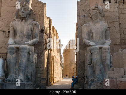 Seduto colossi figure di Ramses II al primo pilone entrata al Tempio di Luxor con locale guide egiziane in attesa per i turisti, Luxor, Egitto, Africa Foto Stock