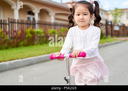 Poco ragazza asiatica Scooter di equitazione Foto Stock