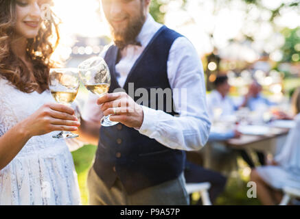 Sposa e lo sposo tintinnanti bicchieri al ricevimento di nozze al di fuori nel cortile. Foto Stock