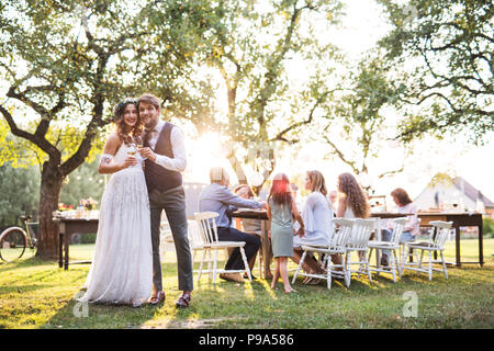 Sposa e lo sposo tintinnanti bicchieri al ricevimento di nozze al di fuori nel cortile. Foto Stock