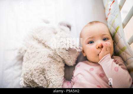 Un bambino ragazza distesa in un lettino in camera da letto a casa, un dito nella sua bocca. Foto Stock