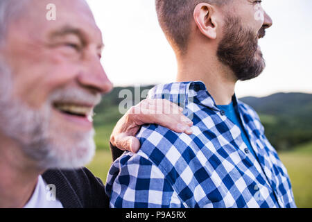 Un adulto hipster figlio col padre senior in una passeggiata nella natura al tramonto. Foto Stock