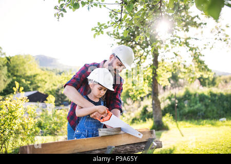 Padre e figlia piccola con una sega al di fuori, il taglio del legno. Foto Stock