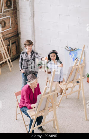 A piena lunghezza ritratto femminile di insegnante di arte la visione di un gruppo di studenti di pittura presso i cavalletti in classe d'arte, spazio di copia Foto Stock