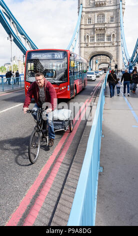 Testa sulla visualizzazione verticale di un ciclista in procinto di essere superato da un London bus rosso che viaggiano attraverso il Tower Bridge Foto Stock