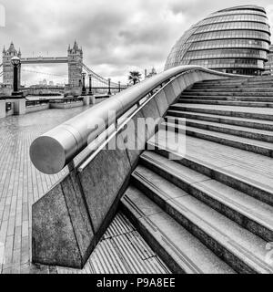 Close up ritratto in bianco e nero vista di gradini e corrimano che conducono ai ristoranti e al Municipio di più di Londra, il Tower Bridge a sinistra Foto Stock