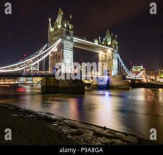 Vista del ponte della torre illuminata di notte dalle sponde del fiume Tamigi, Londra, con il Gherkin nella distanza Foto Stock