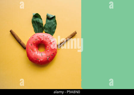 Una ciambella di creativi con le orecchie di foglie che assomigliano a un coniglio su uno sfondo colorato in stile minimale. Foto Stock