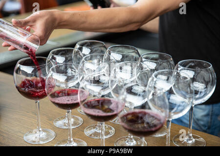 Versando il vino rosso dal decanter nella Wineglass sulla fila di bicchieri. Close up di vino rosso alla cantina di servizio per far festa o evento. Foto Stock