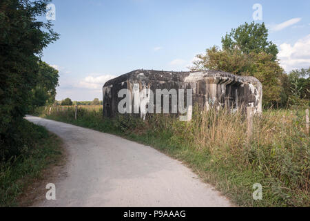 Un abbandonato la guerra mondiale due bunker si siede accanto a un paese rurale strada attraverso terreni agricoli in Belgio in una giornata di sole. Foto Stock
