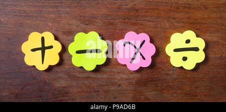 Scuola di concetto di matematica. Sticky note colorate a forma di fiore isolato con i simboli matematici su sfondo di legno. Foto Stock
