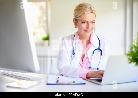 Femmina matura medico usando il suo computer portatile mentre è seduto all'ufficio del medico. Foto Stock