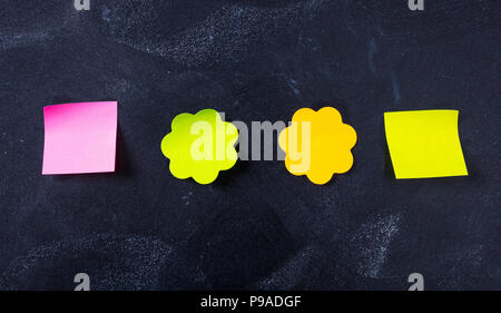 Il concetto di scuola. Sticky note colorate in varie forme con copia spazio sulla lavagna sfondo. Foto Stock