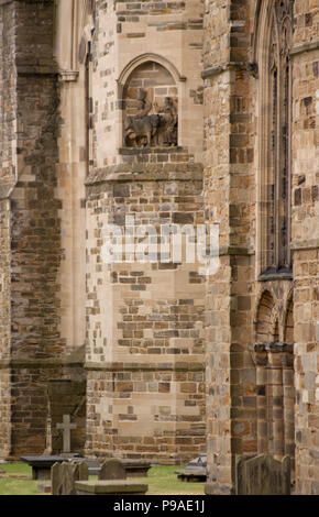 Dun statura di vacca intagliare sulla parete esterna della Cattedrale di Durham Regno Unito Inghilterra con antiche tombe nel cimitero Foto Stock