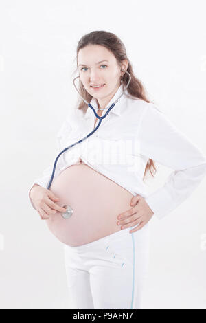 Donna incinta ascoltando attraverso uno stetoscopio che fa di lei un bambino Foto Stock