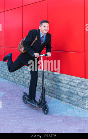 Allegro imprenditore corse rapidamente un kick scooter dalla parete rossa Foto Stock