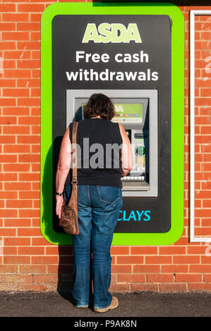 Una donna con un free cash macchina al di fuori di un supermercato Asda. Foto Stock