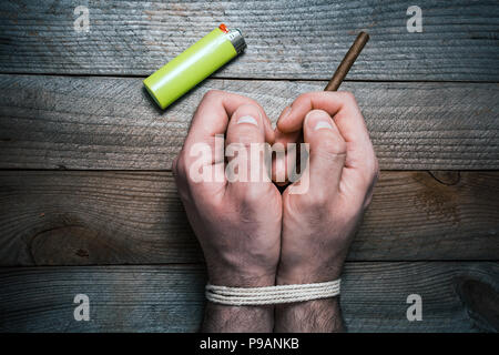 Smettere di fumare concetto con 2 legato le mani su di un tavolo di legno accanto ad un accendino. La mano destra è in possesso di una sigaretta Foto Stock