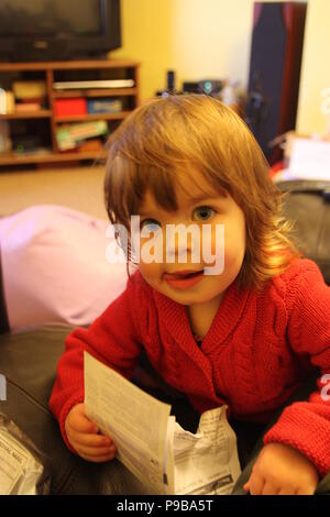 Ragazza giovane con occhi blu e capelli con stile in un rosso cardigan seduta su una poltrona in pelle di concentrare la lettura con la sua linguetta sporgente Foto Stock