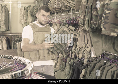 Maschio Serios cliente scegliere giubbotto antiproiettile nell esercito store Foto Stock