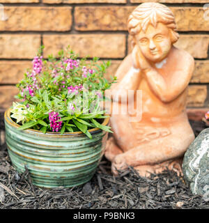 Un giardino di pietra di un cherubino accanto a una pentola di rosa fiori Angelonia da un muro di mattoni. Stati Uniti d'America Foto Stock