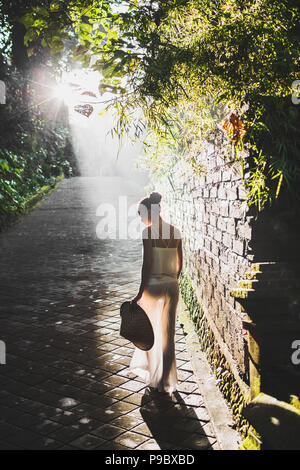 Giovane donna slim camminando sulla vecchia strada nel bel mattino raggi solari, incredibile natura di Bali e antichi di architettura Foto Stock