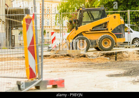 Orange draga in corrispondenza di un sito di costruzione nella città. La costruzione della rete fognaria nella zona. Parcheggiate le macchine di lavoro sulla strada. Bulldozer sul sito. Strada interrotta Foto Stock