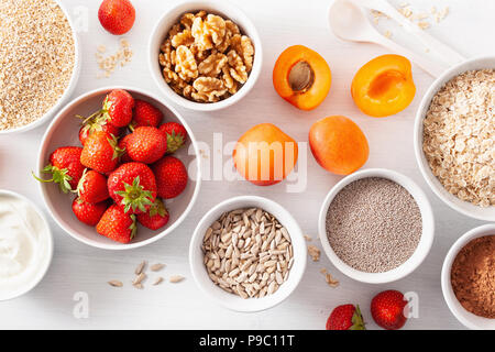 Varietà di materie di cereali, frutta e noci per la prima colazione. Fiocchi di avena e di acciaio tagliati, orzo, noce, chia, albicocca, fragola. Ingredienti sani Foto Stock