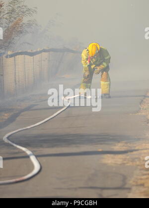 Melbourne, Australia - 13 Aprile 2018: Fire fighter con un tubo flessibile in corrispondenza di una bussola incendio in un'area suburbana di Knox City a est di Melbourne. Foto Stock