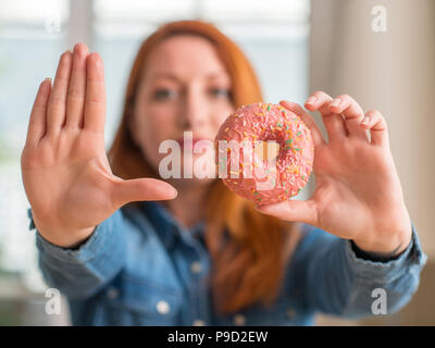 Redhead donna ciambella di contenimento a casa con la mano aperta facendo segno di stop con gravi e fiducioso espressione, gesto di difesa Foto Stock