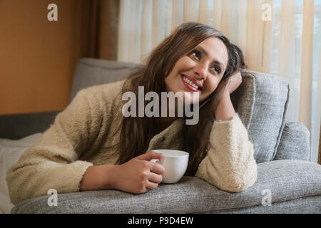 Giovane donna con tazza di caffè sul divano Foto Stock