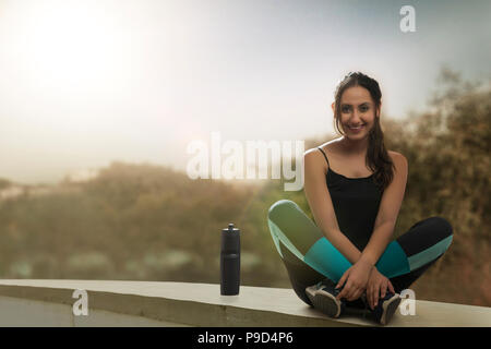 Runner donna seduta gambe incrociate con una bottiglia d'acqua sulla parete Foto Stock