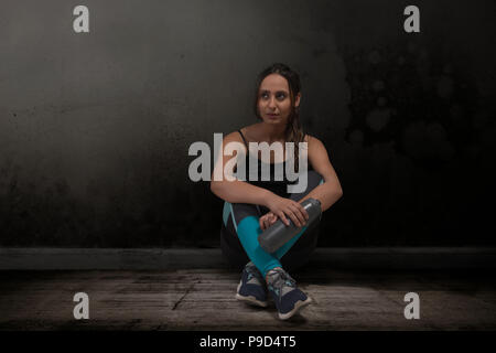 Runner donna seduta gambe incrociate con bottiglia di acqua sul pavimento Foto Stock