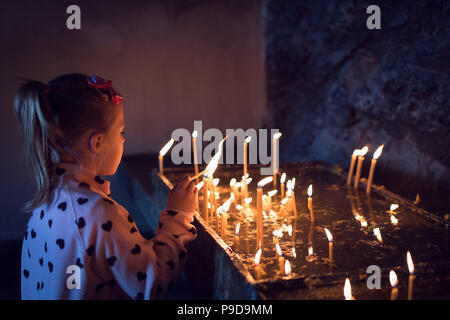 Grazioso piccolo ragazza caucasica alleggerimento del memorial candele nel monastero Foto Stock